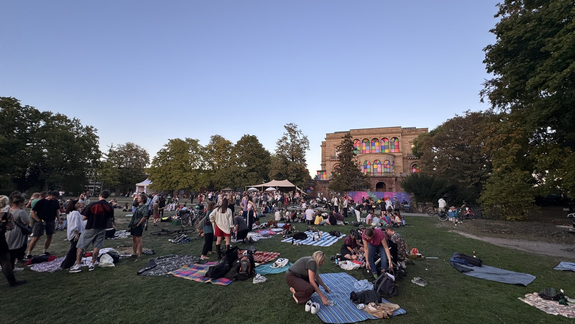 Viele Menschen sitzen und tanzen auf der Wiese im Park der Villa Berg, im Hintergrund die Villa und ein Stretchzelt