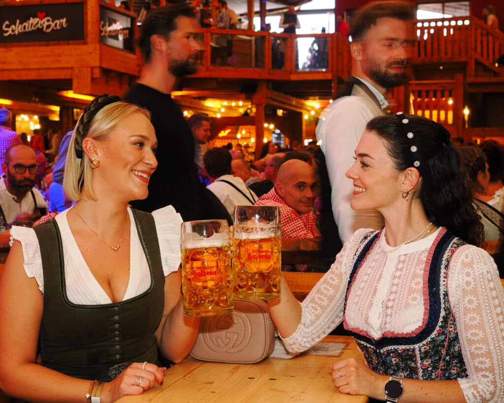 Zwei Frauen im Dirndl stoßen im Festzelt Sonja Merz mit Maßkrügen an