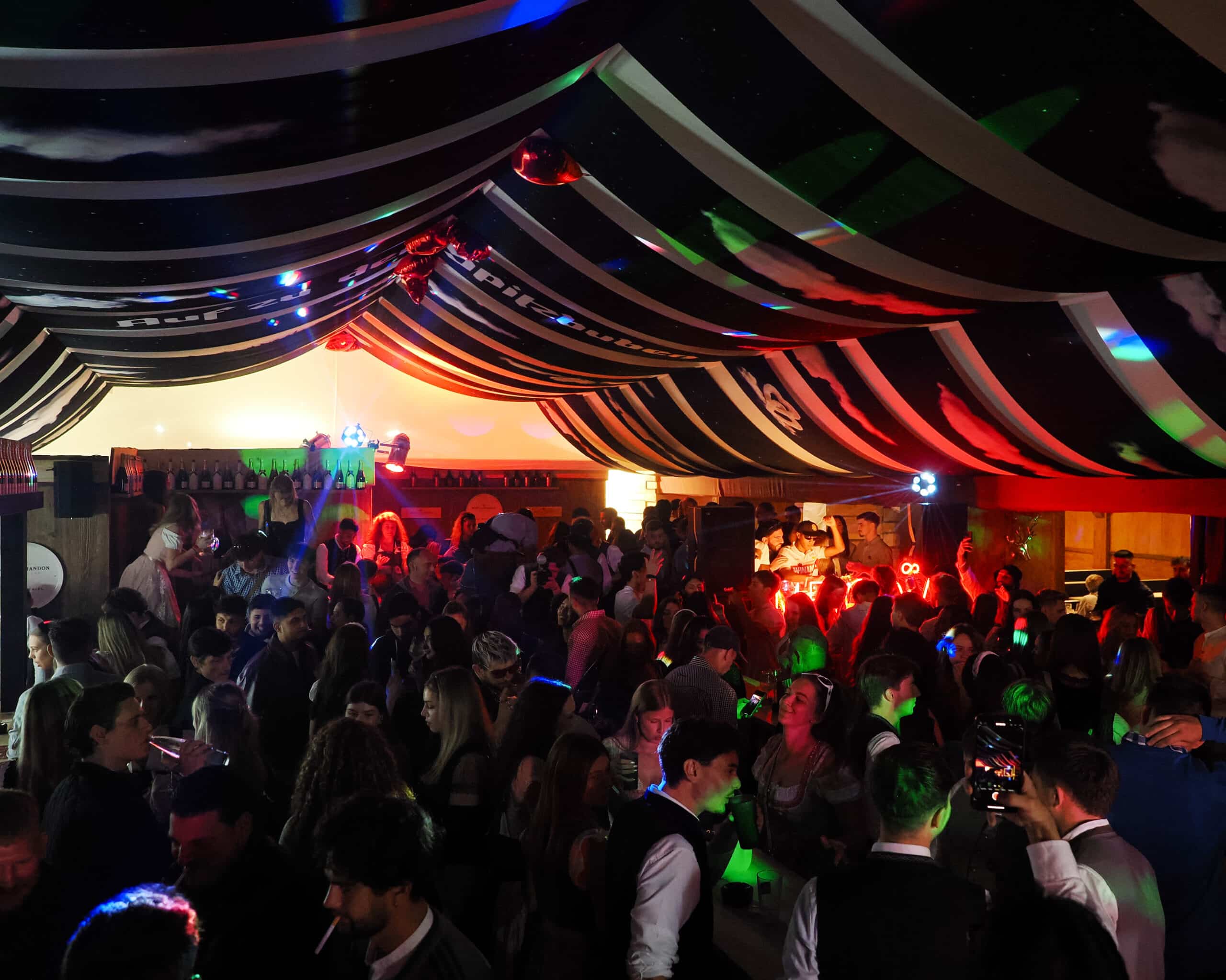Tanzende Gäste und DJ-Pult im Club Spitzbuben Lodge unter schwarz-weißem Zelthimmel