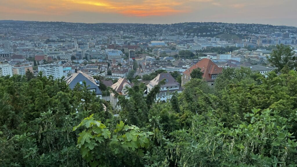 Blick über den Stuttgarter Kessel bei Sonnenuntergang, im Vordergrund grüne Bäume